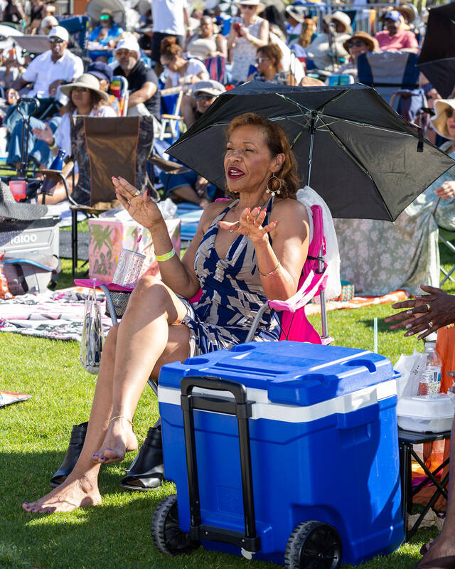 A member applauding from her chair under a shade umbrella at a Palm Springs festival